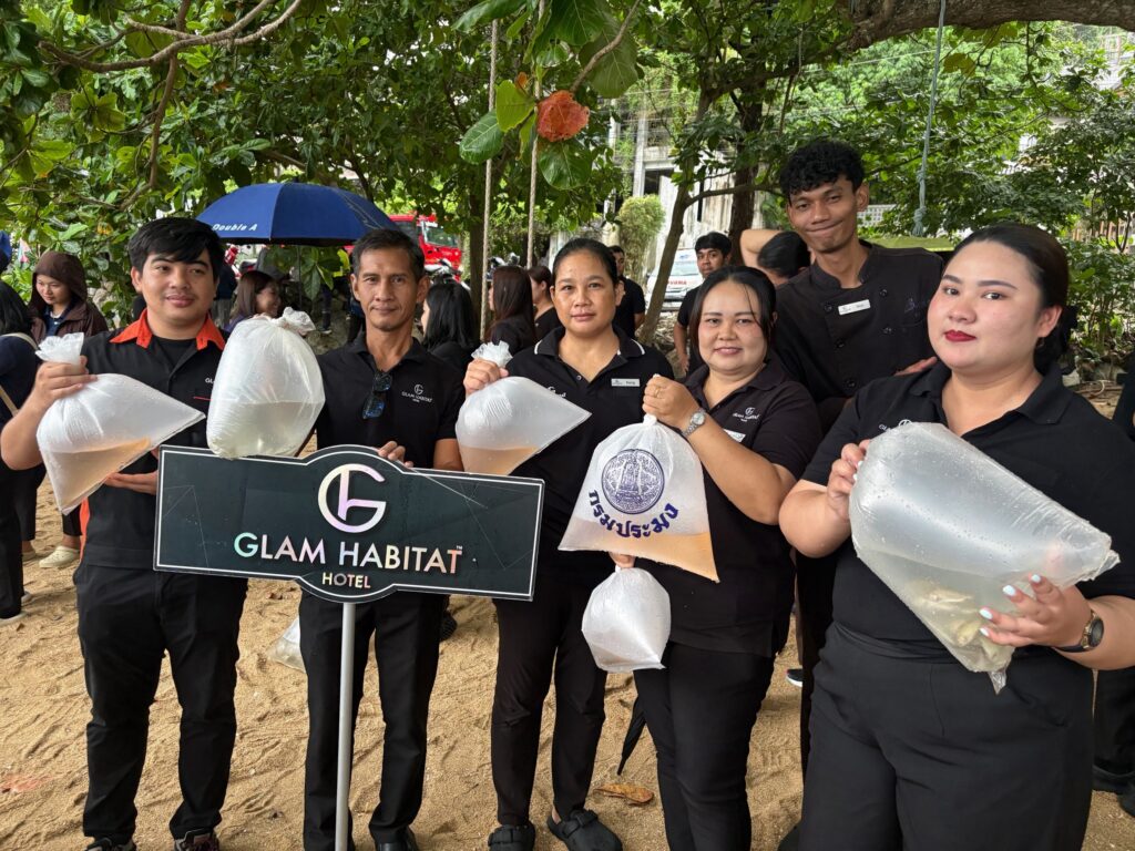 Glam Habitat team members holding bags of fish fry beside the hotel sign at Kamala's 2026 aquatic life release event