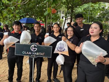 Glam Habitat team members holding bags of fish fry beside the hotel sign at Kamala's 2026 aquatic life release event