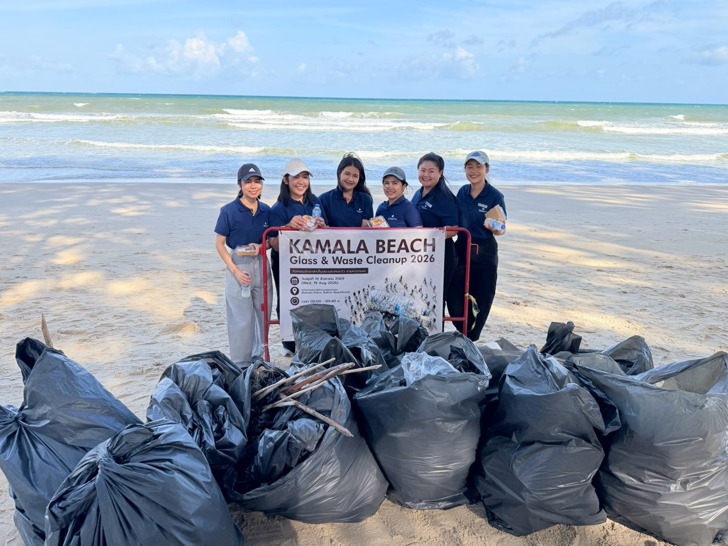 Glam Habitat Hotel team members posing with the Kamala Beach Glass & Waste Cleanup 2026 banner and bags of collected beach waste