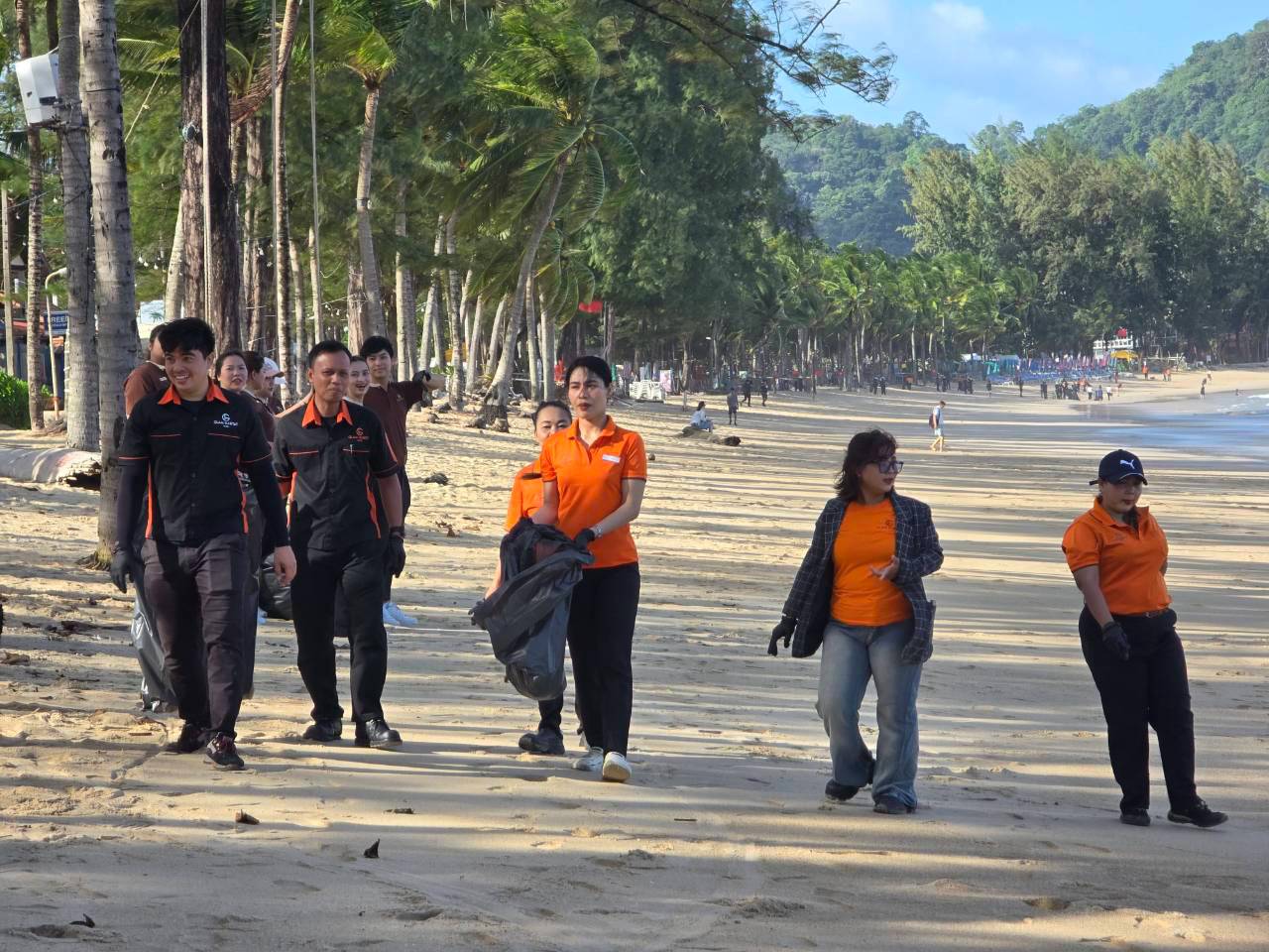 Hotel staff walking along Kamala Beach carrying bags of collected waste