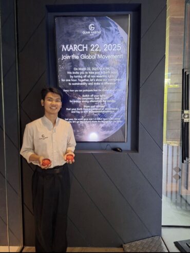 A Glam Habitat Hotel team member holding candles beside the Earth Hour 2025 invitation display at the hotel entrance
