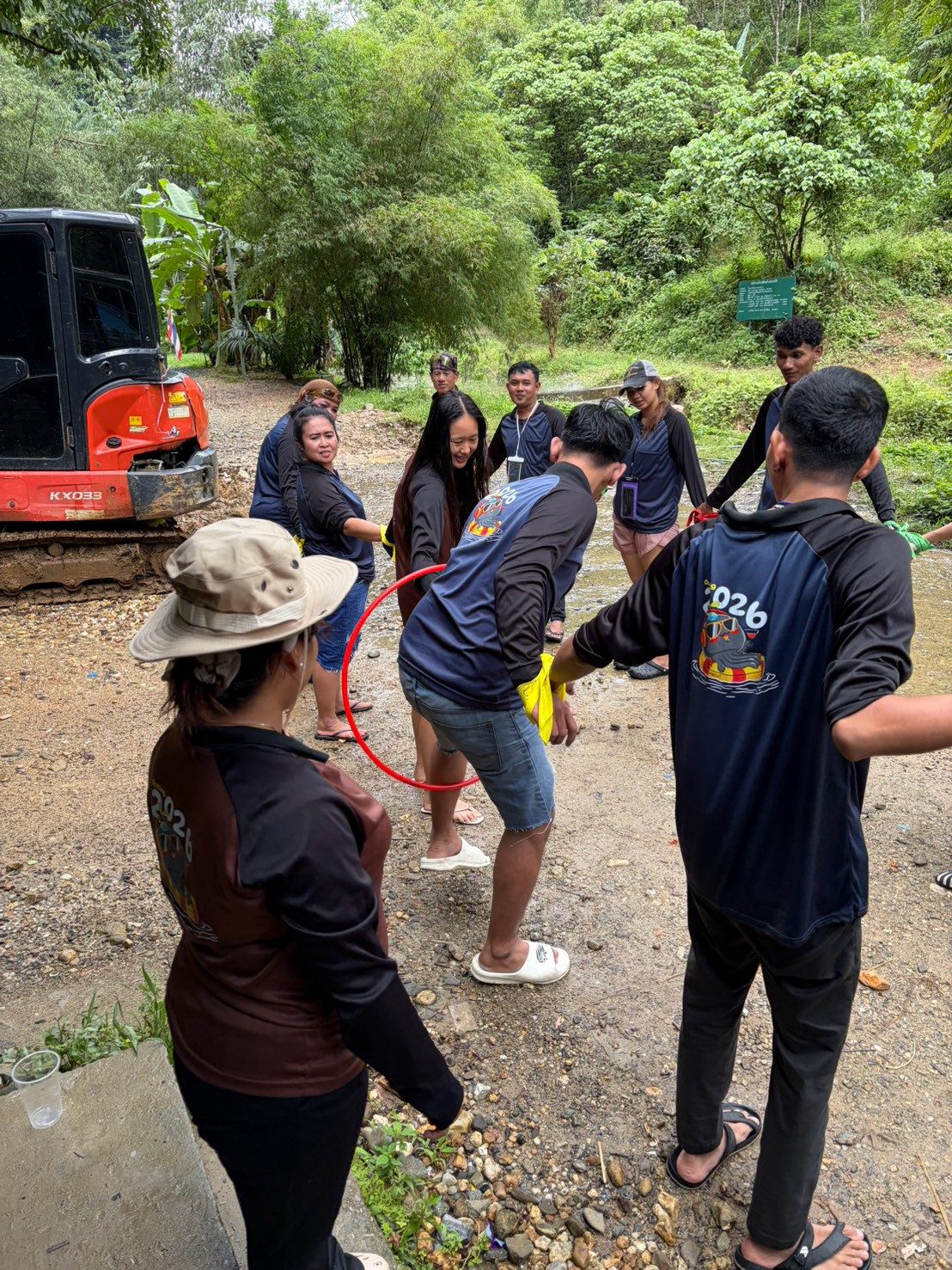 Glam Habitat staff playing a hula hoop passing game at a rest stop during Outing 2026, with the "Outing 2026" jersey logo visible