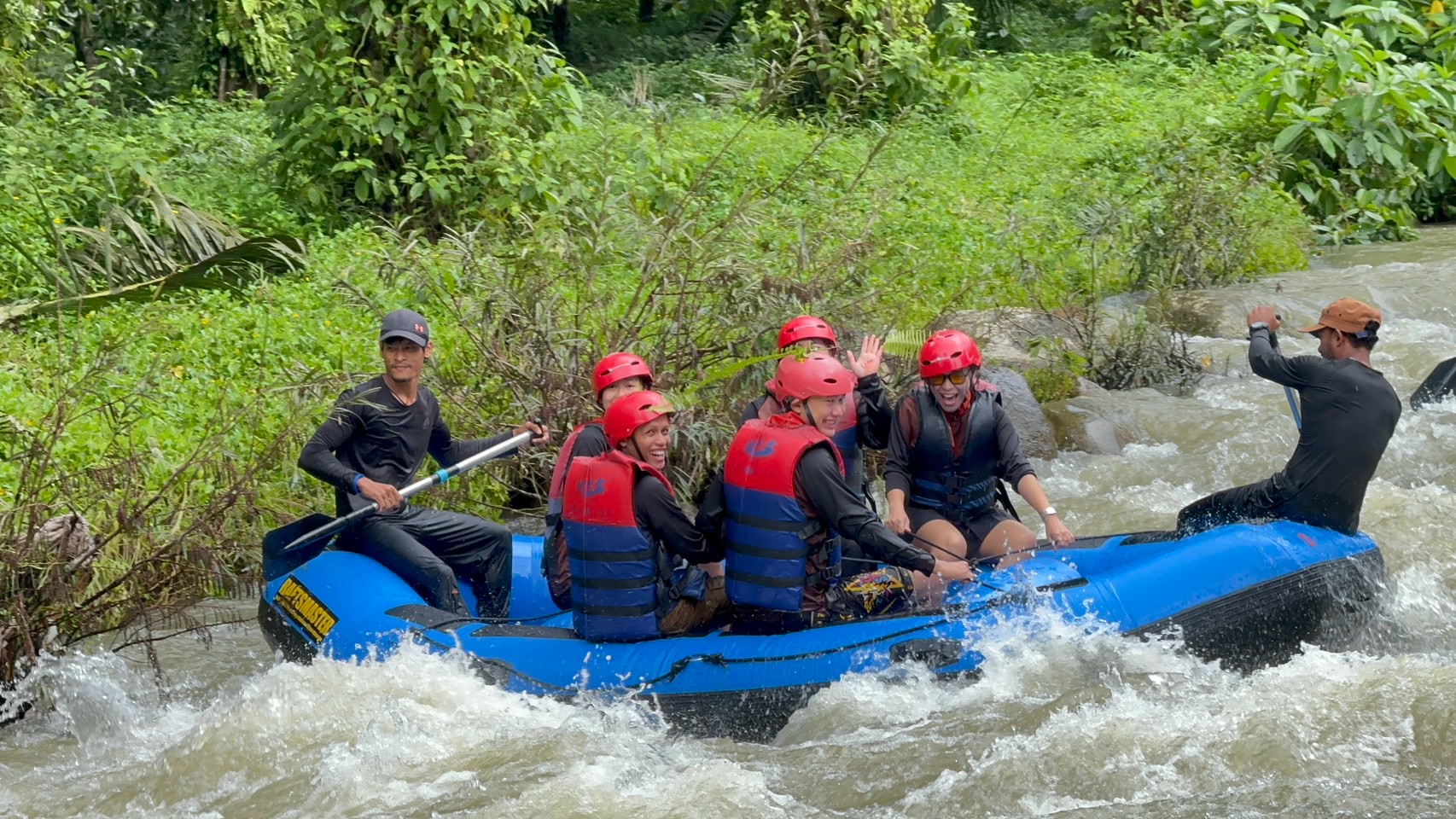 The Glam Habitat rafting team cheering and waving mid-rapid on the white-water rafting leg of Outing 2026