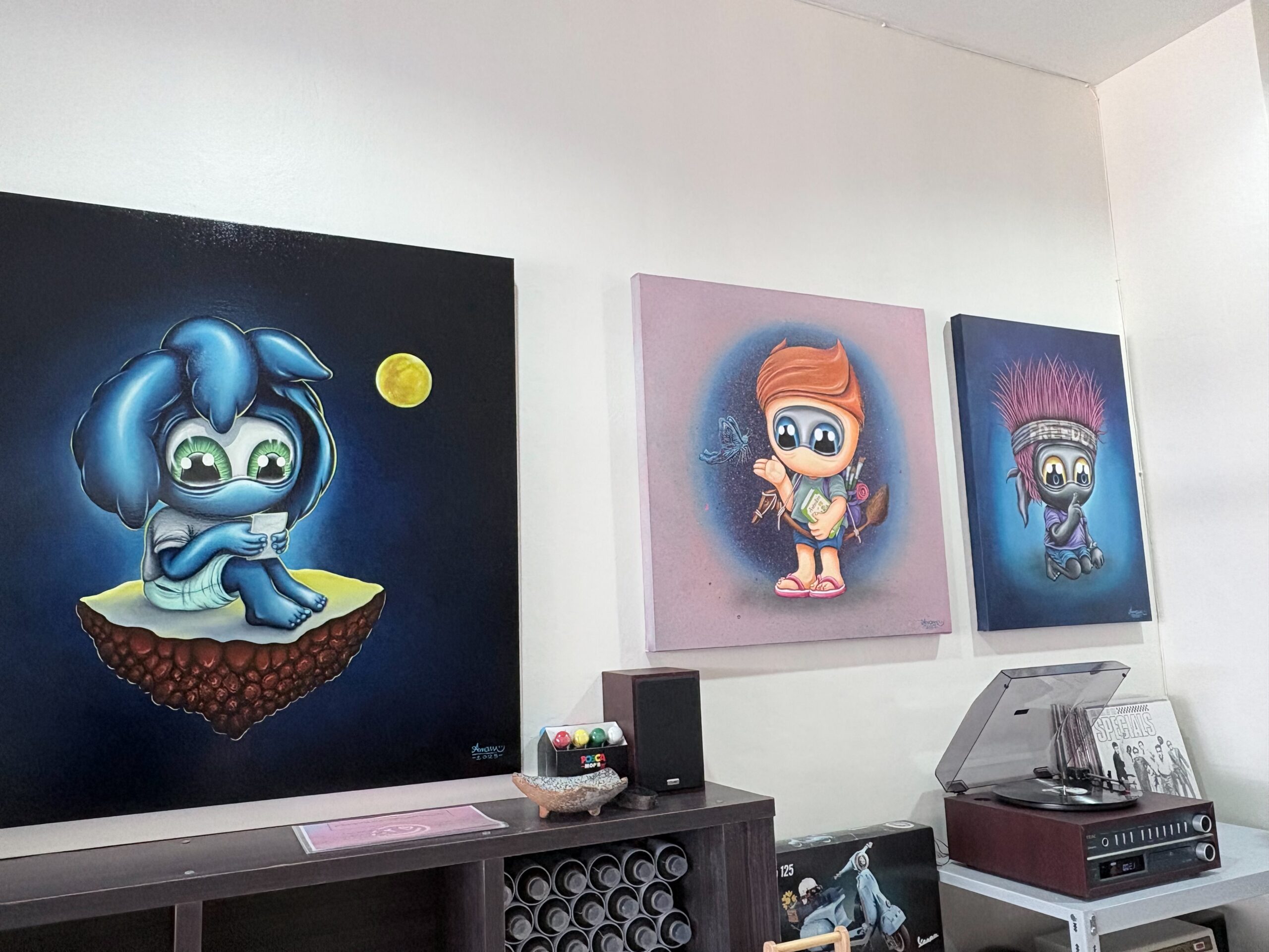 Three MUTE character paintings by Amann displayed on a studio wall in Phuket