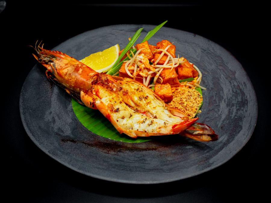 Grilled giant prawn with lemon and a noodle garnish on a banana leaf