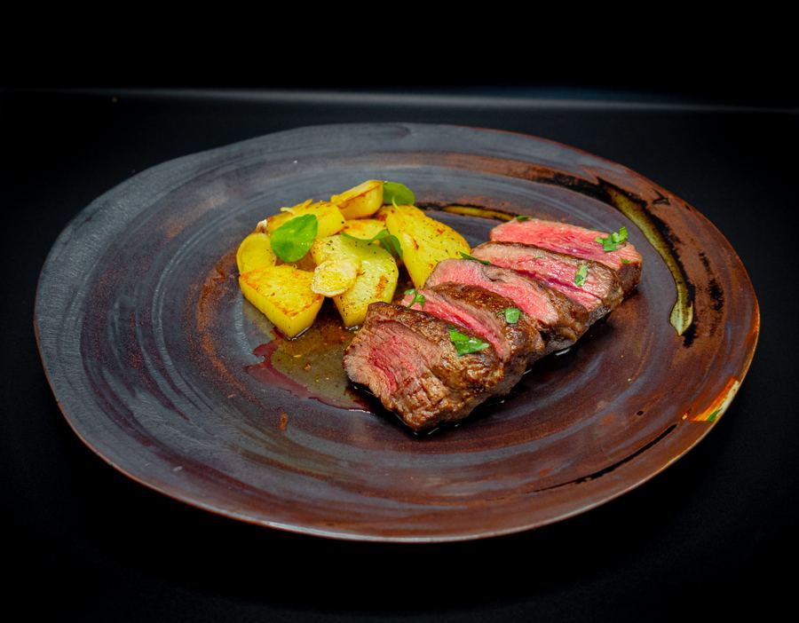 Sliced medium-rare beef with roasted potatoes on a dark stoneware plate