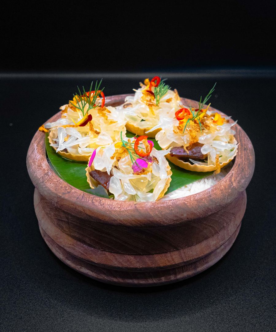 Garnished pastry tartlets arranged on a leaf in a turned wooden bowl