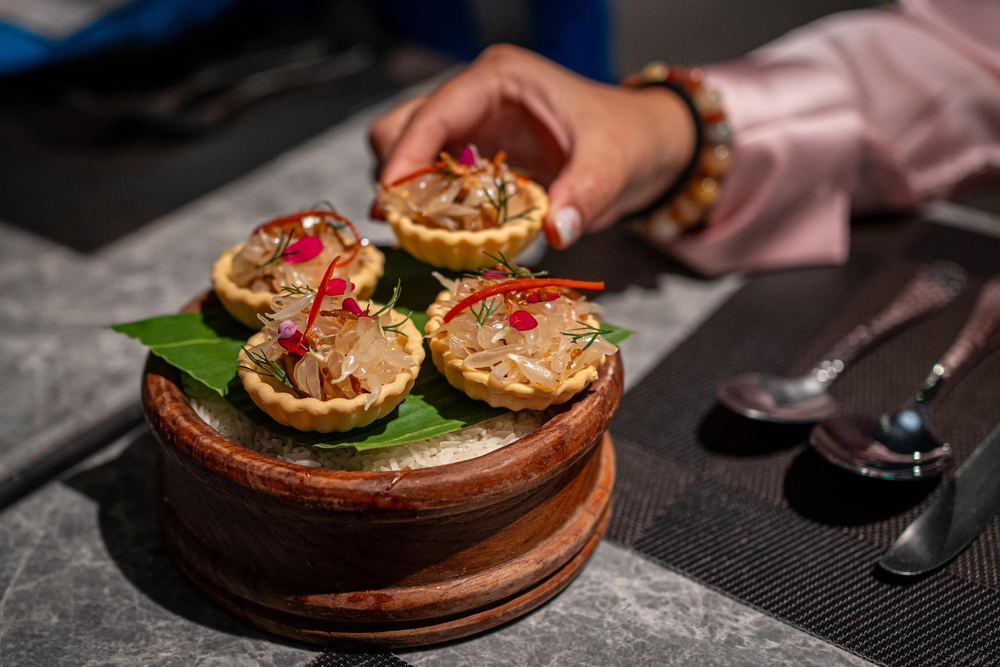 Guest reaching for a delicately garnished pastry tartlet served in a wooden bowl