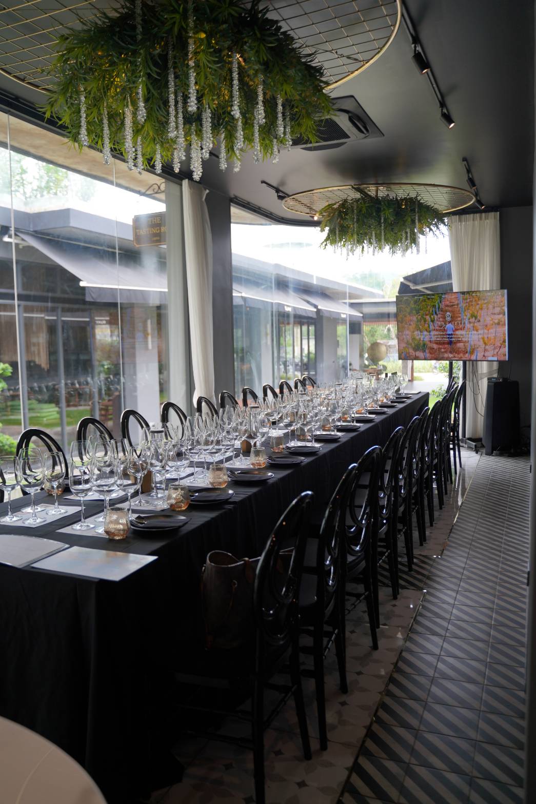 A long tasting table set with rows of wine glasses under hanging greenery, ready for the Villa Saletta wine masterclass