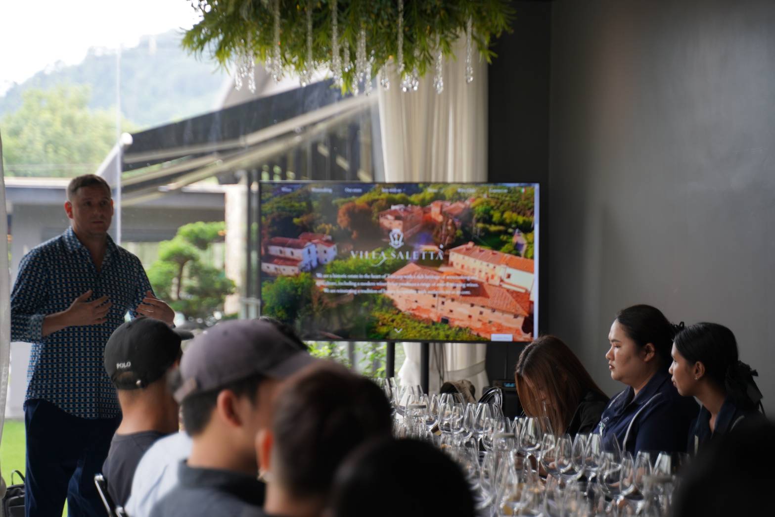 The Villa Saletta estate shown on screen as the wine masterclass begins, with hospitality guests seated at the tasting table