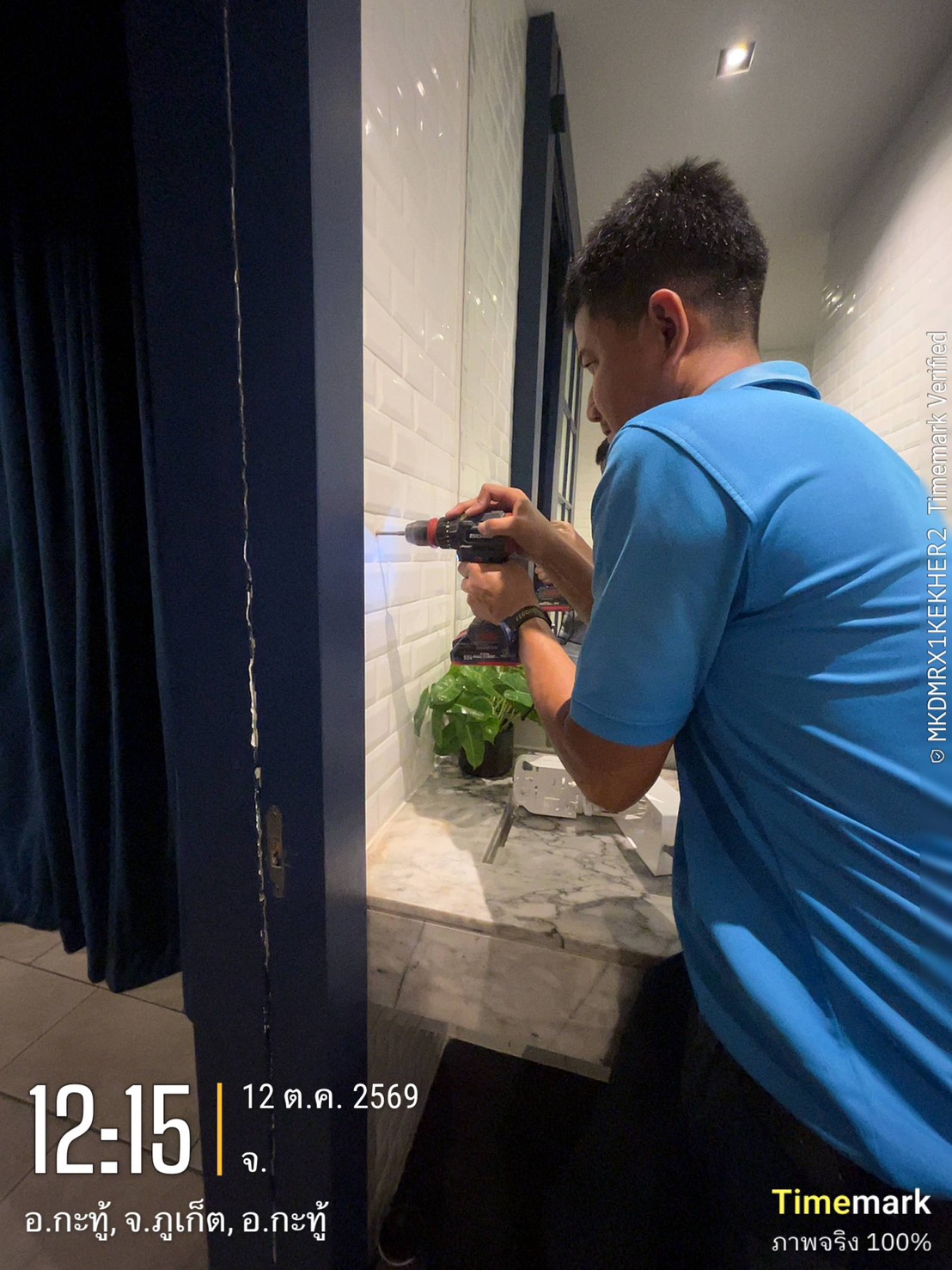 An ECOLAB technician drilling into white subway tiles to mount a hand soap dispenser in a Glam Habitat restroom
